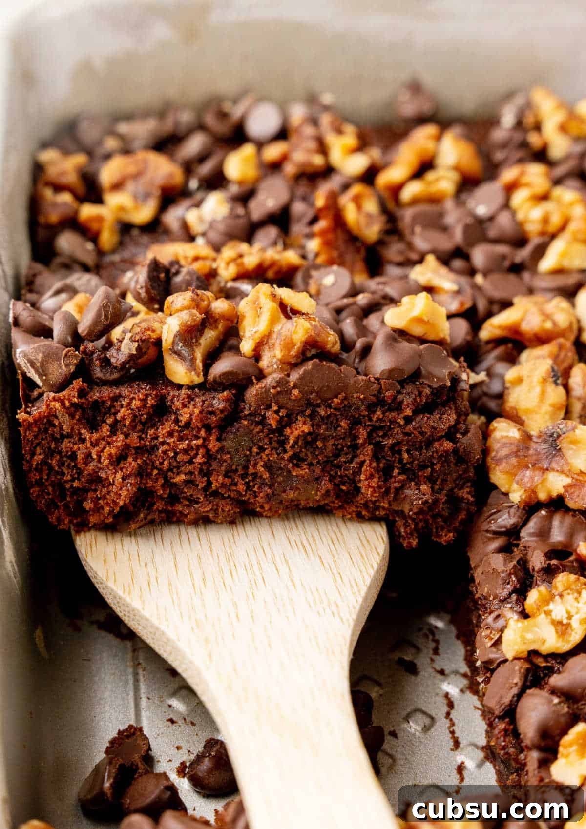 Decadent Chocolate and Date Cake Recipe for Moist Loaves 3 Wooden spatula lifting piece of date cake with chocolate chips and walnuts from the pan.
