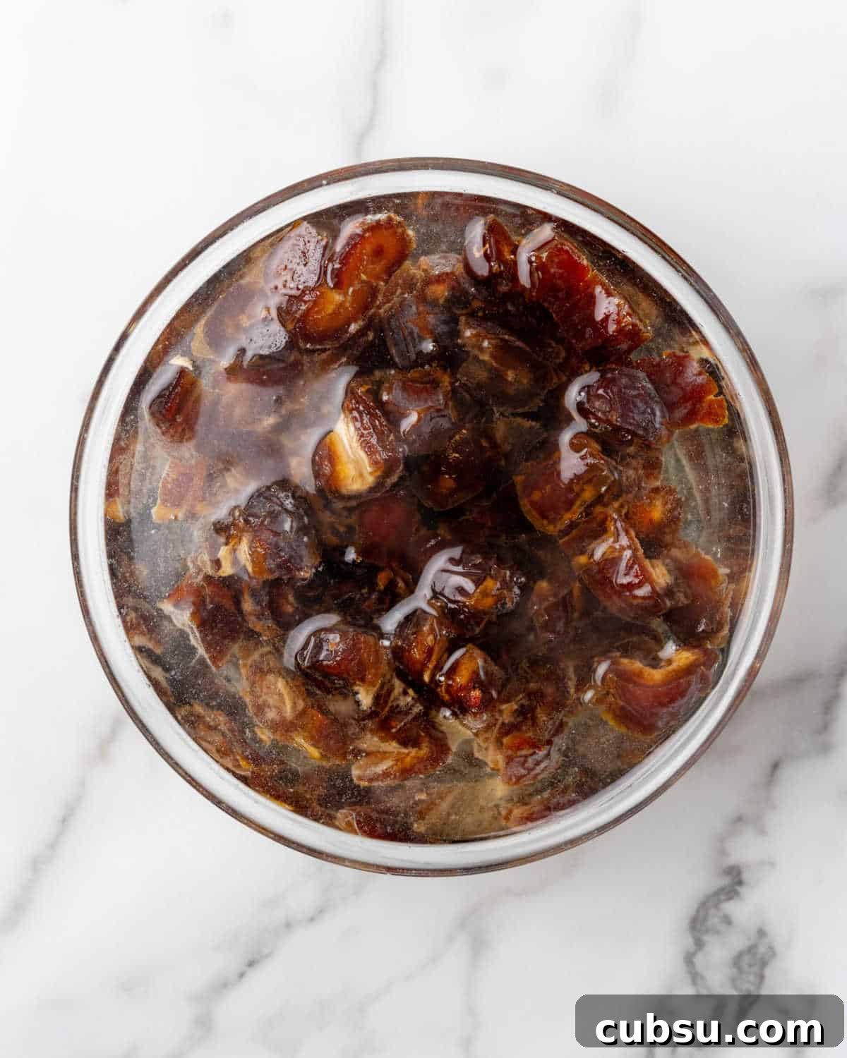 Decadent Chocolate and Date Cake Recipe for Moist Loaves 7 Date covered in water in a glass bowl on a white marble surface.