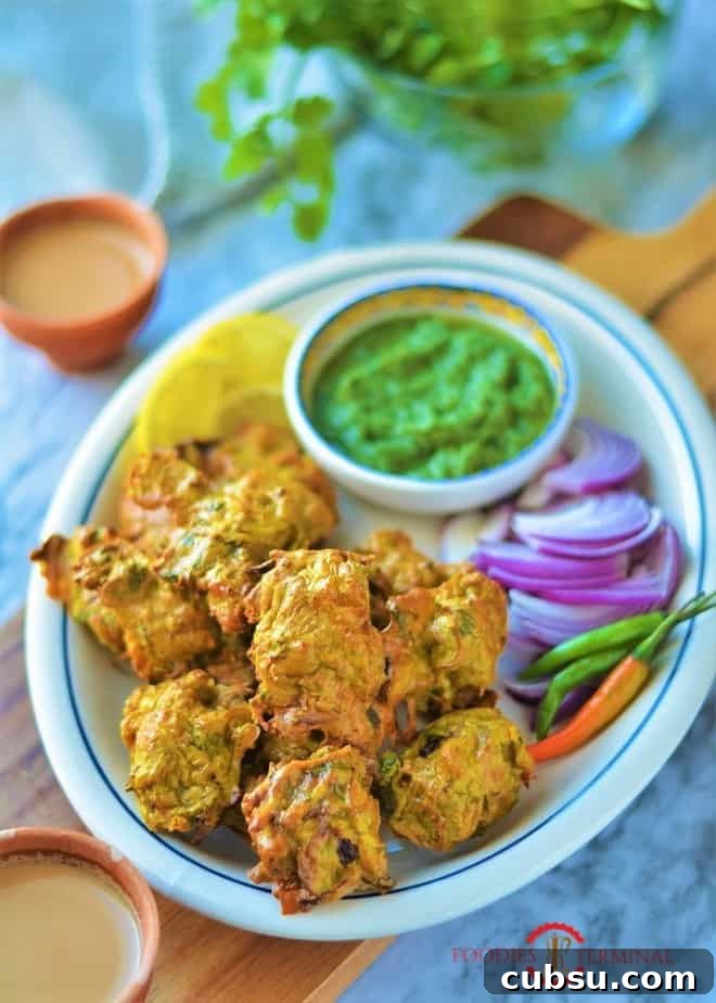 Chicken Pakora on a white oval plate with blue rim with onion slices, green chilies, green chutney