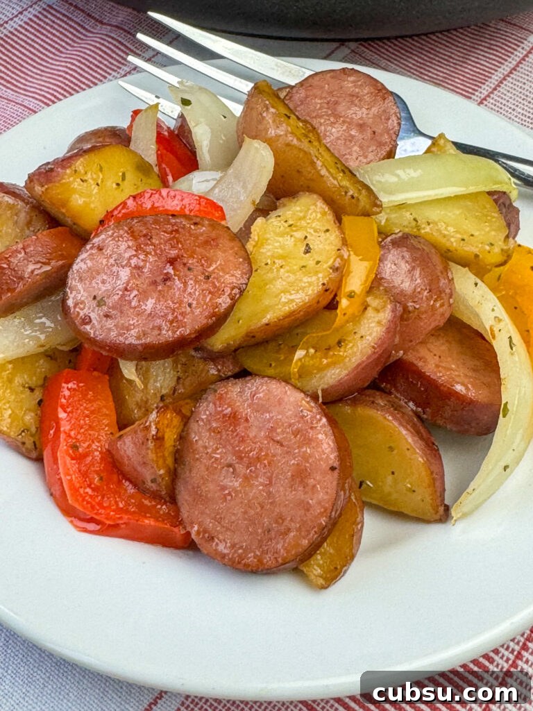Brown coins of Kielbasa nestled among tender potatoes with a light seasoning on a white plate with a fork in the background.