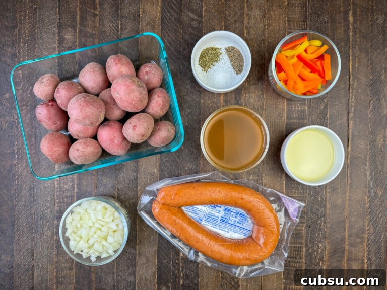 Ingredients to make a kielbasa recipe is Kielbasa sausage, baby red potatoes, onions, bell peppers, vegetable oil, chicken stock, salt, pepper and Italian seasoning on a wooden counter top.