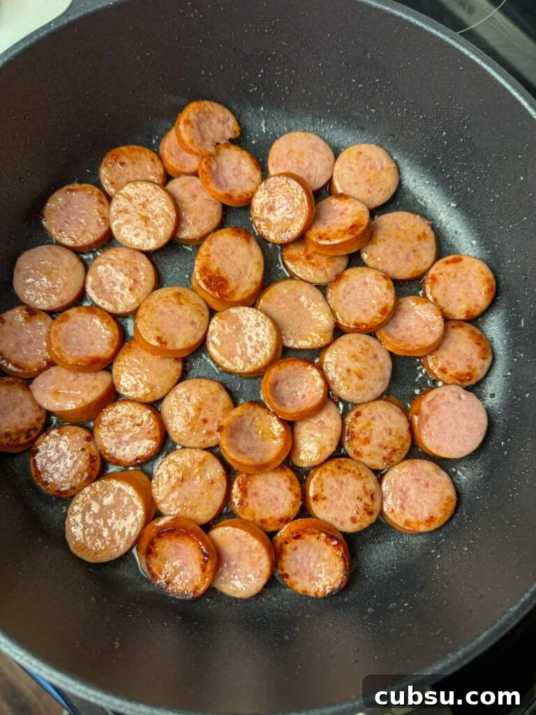 Browned slices of Kielbasa in vegetable oil in a skillet.