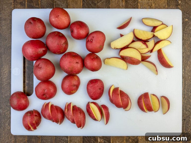Baby red potatoes in a variety of different stages on a white cutting board showing how to cut the potatoes to fry in a skillet.