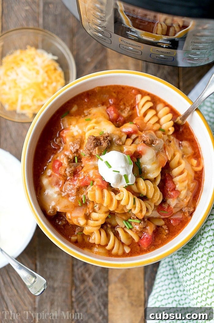 A bowl of cheesy taco pasta with rotini, topped with sour cream, sits enticingly next to a tempting bowl of shredded cheese and the very Instant Pot that crafted this delightful instant pot taco casserole.