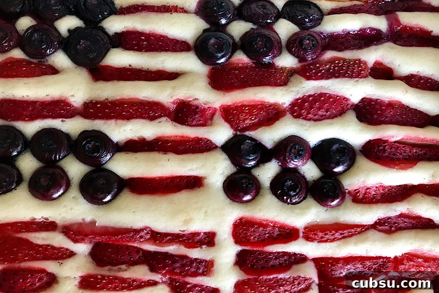 Red, White & Blue Fruit-Topped American Flag Cake Recipe 5 a close up picture of baked blueberries and sliced strawberries baked into a white flag cake