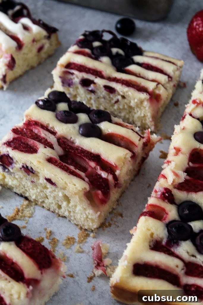 Red, White & Blue Fruit-Topped American Flag Cake Recipe 6 slices of american flag cake made with blueberries and strawberries with a strawberry in the background and a cake pan
