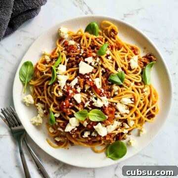 A plate of bolognese sprinkled with feta cheese and fresh basil