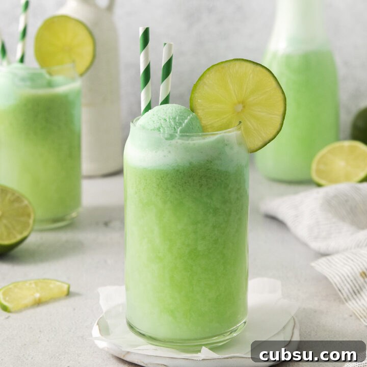 a can shaped glass filled with lime sherbet punch. It's garnished with lime wedges and two green and white straws.