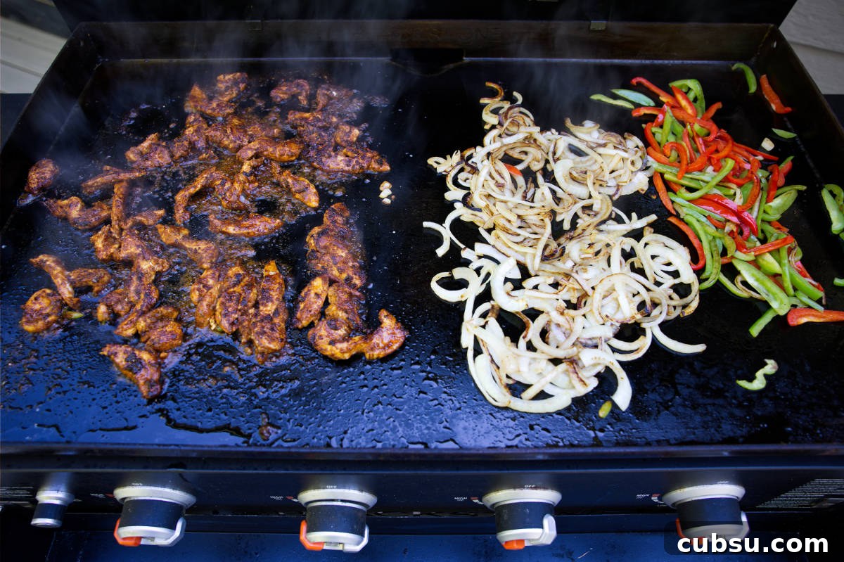 Blackstone Griddle Steak Fajitas: Flavorful Skillet Recipe 8 Cooking fajitas on the Blackstone griddle, with chicken, onions, and bell peppers in separate piles.
