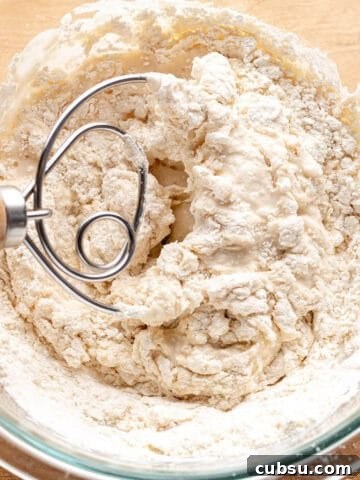 A glass bowl with a sourdough starter and danish dough whisk mixing it together.