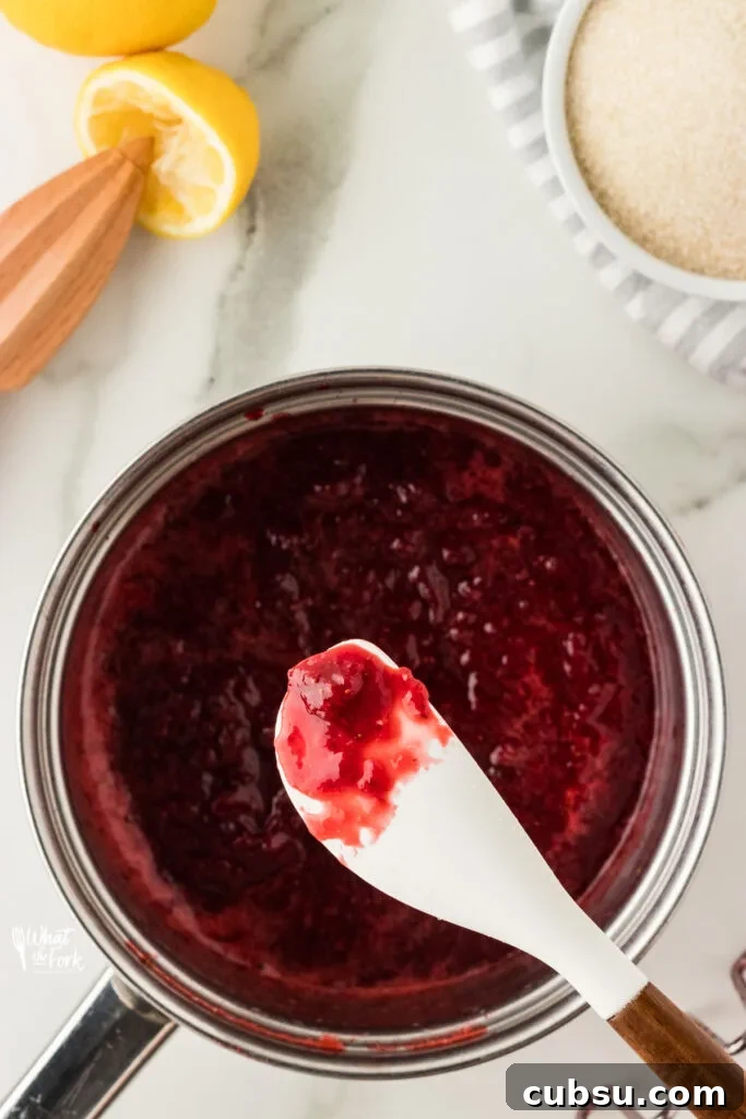 3-Ingredient Strawberry Cake Filling Recipe for Fresh Flavor 6 strawberry cake filling cooked in a silver saucepan with some on a white silicone spatula to show how thickened it is.