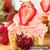 a gluten free vanilla cupcake filled with an easy 3-Ingredient Strawberry Cake Filling. The cupcake is cut open to show the filling and is topped with strawberry frosting and half of a fresh strawberry.