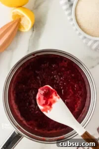 3-Ingredient Strawberry Cake Filling Recipe for Fresh Flavor 10 strawberry cake filling cooked in a silver saucepan with some on a white silicone spatula to show how thickened it is.