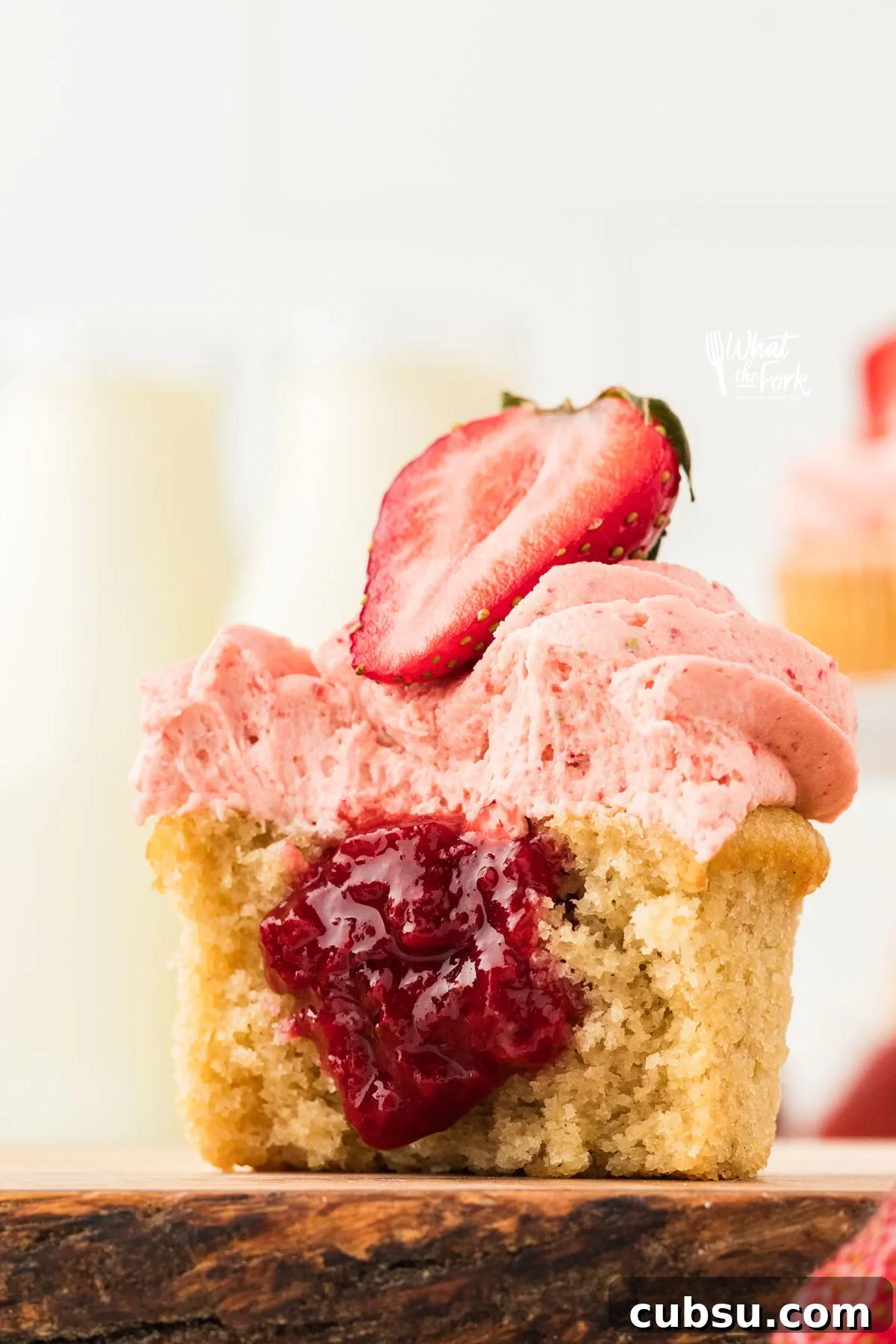 3-Ingredient Strawberry Cake Filling Recipe for Fresh Flavor 3 a gluten free vanilla cupcake filled with an easy 3-Ingredient Strawberry Cake Filling. The cupcake is cut open to show the filling and is topped with strawberry frosting and half of a fresh strawberry.