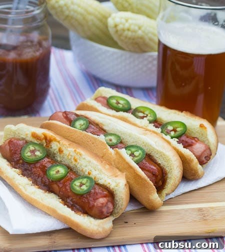 Hot Dogs on a wooden cutting board with beer and corn in background.