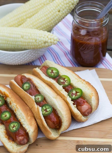 Dr Pepper BBQ Hot Dogs with Tangy Cola Glaze 4 Three Hot Dogs with Dr Pepper Barbecue Sauce with corn in background.