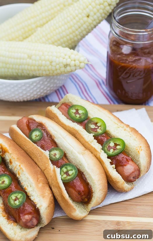 Dr Pepper BBQ Hot Dogs with Tangy Cola Glaze 6 Hot Dogs with Dr. Pepper BBQ Sauce and corn in background.
