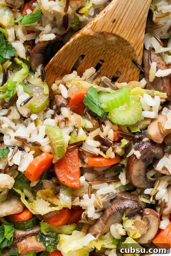 Crispy Oven and Air Fryer Rice: Step-by-Step Guide for Crunchy Rice 12 Top down shot of a wooden spoon sticking out of a pan of wild rice pilaf with carrots, celery and chopped parsley.