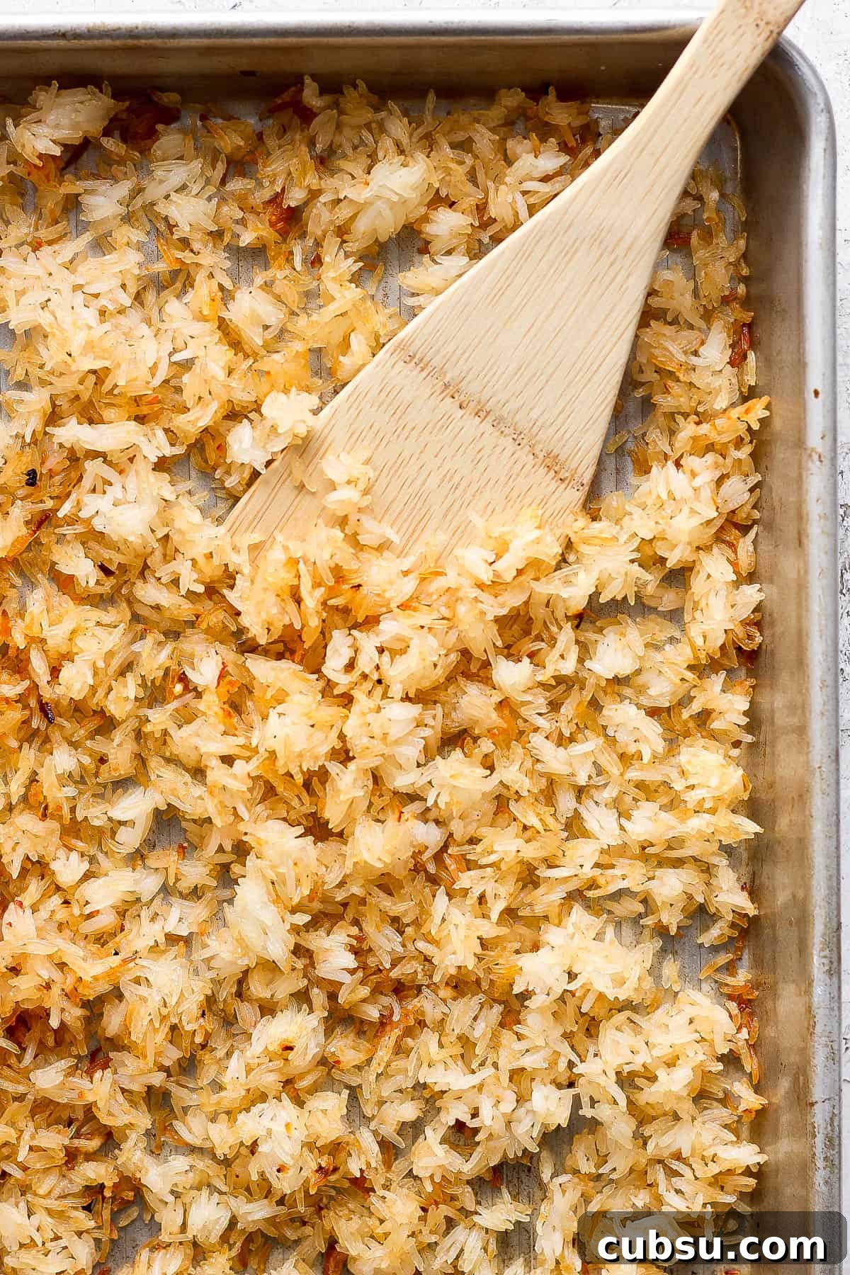 Crispy Oven and Air Fryer Rice: Step-by-Step Guide for Crunchy Rice 5 Crispy rice on a sheet pan with a wooden spatula.