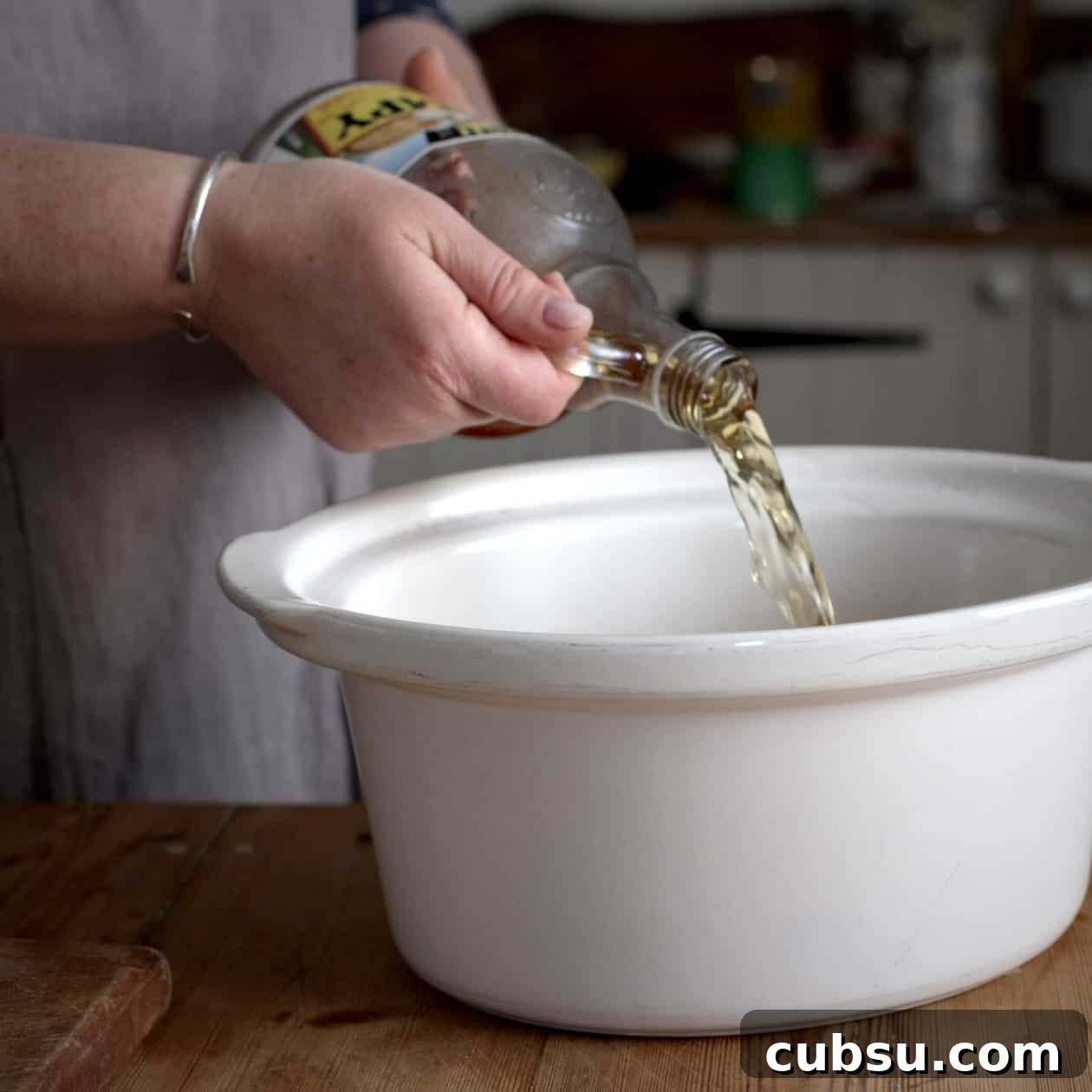 Slow Cooker Pork in Cider and Mustard Sauce 11 Woman pouring cider into a white slow cooker bowl from an old fashioned glass bottle
