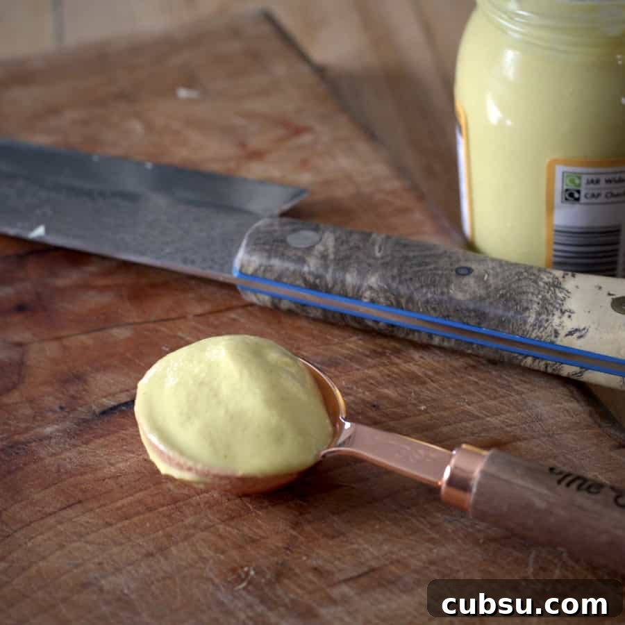 Slow Cooker Pork in Cider and Mustard Sauce 12 A small copper spoon filled with Dijon mustard on a wooden chopping board with a silver knife behind