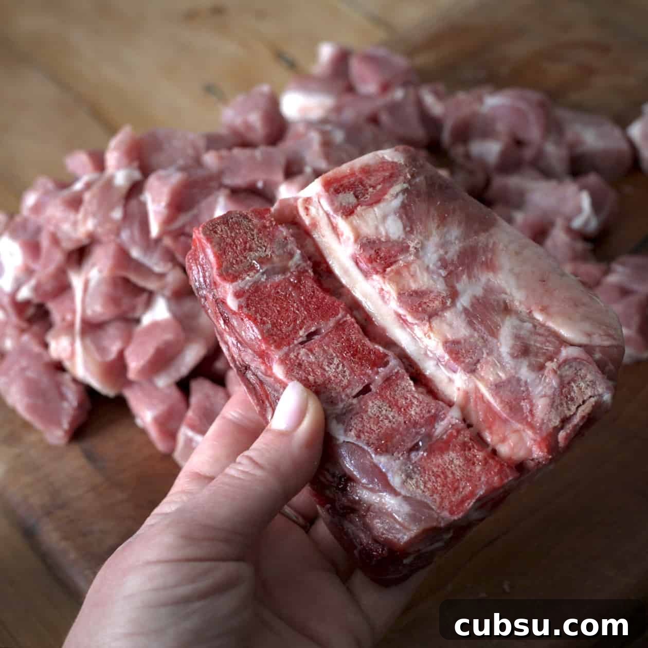 Slow Cooker Pork in Cider and Mustard Sauce 5 Woman’s holding a raw pork bone over a pile of dice pork on a wooden board