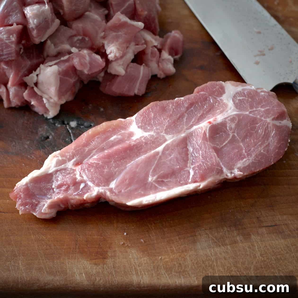 Slow Cooker Pork in Cider and Mustard Sauce 6 Slice of raw pork on a wooden chopping board with a sharp knife behind