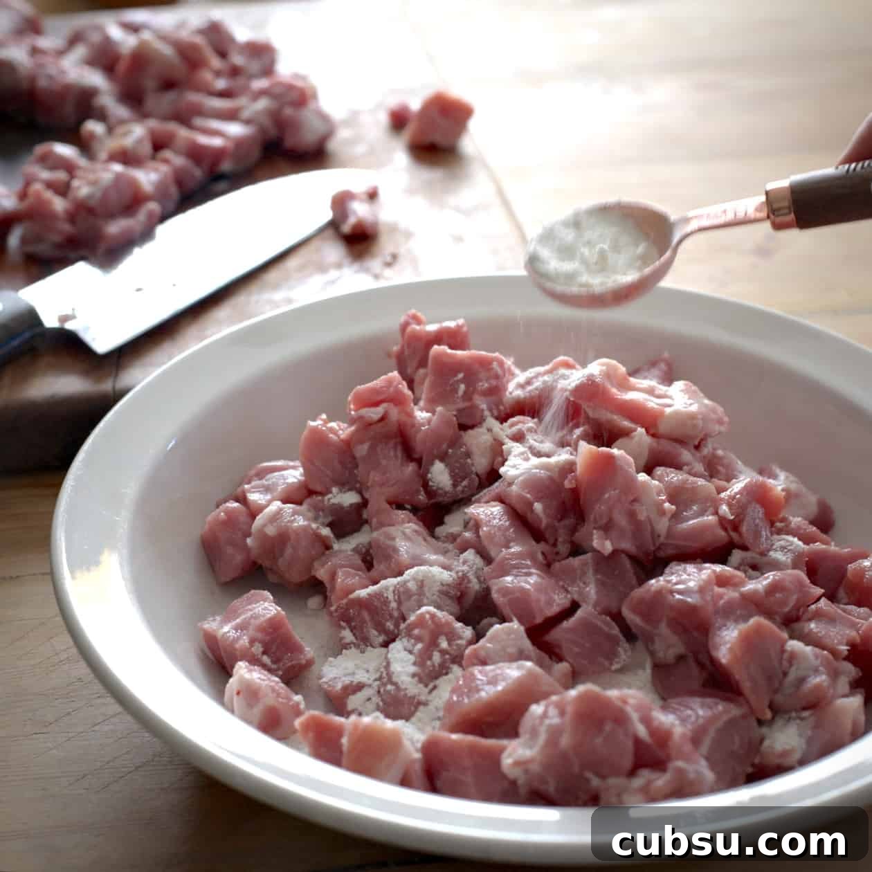 Slow Cooker Pork in Cider and Mustard Sauce 7 A tablespoon of flour being dusted over a white bowl of diced pork before searing