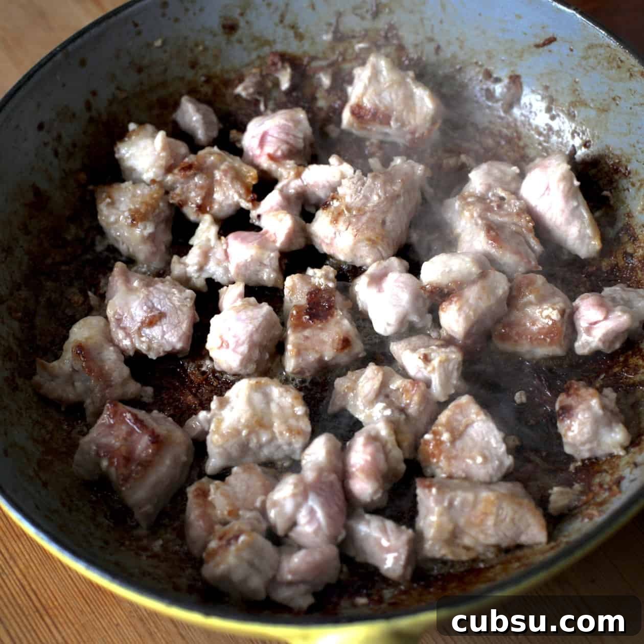 Slow Cooker Pork in Cider and Mustard Sauce 8 Inside shot of a yellow and grey frying pan filled with diced pork that has been partly seared