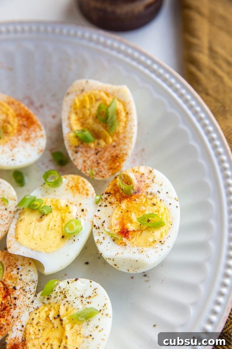 Hard boiled eggs sprinkled with paprika and chopped green onion on a white plate