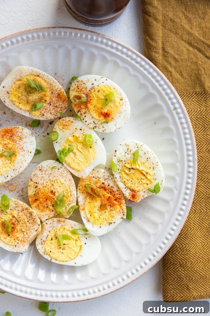 Hard boiled eggs sliced in half and sprinkled with salt, pepper, and paprika and green onions on a white plate
