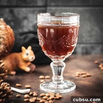 Gorgeous glass filled with maple syrup coffee, placed on dark brown ground, next to squirrel figure.