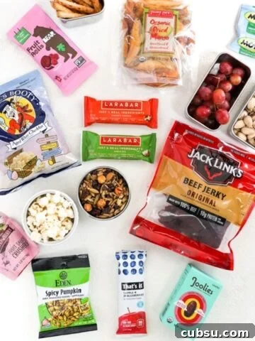 Sixteen different snacks, some packaged, and some in containers, on a white surface.