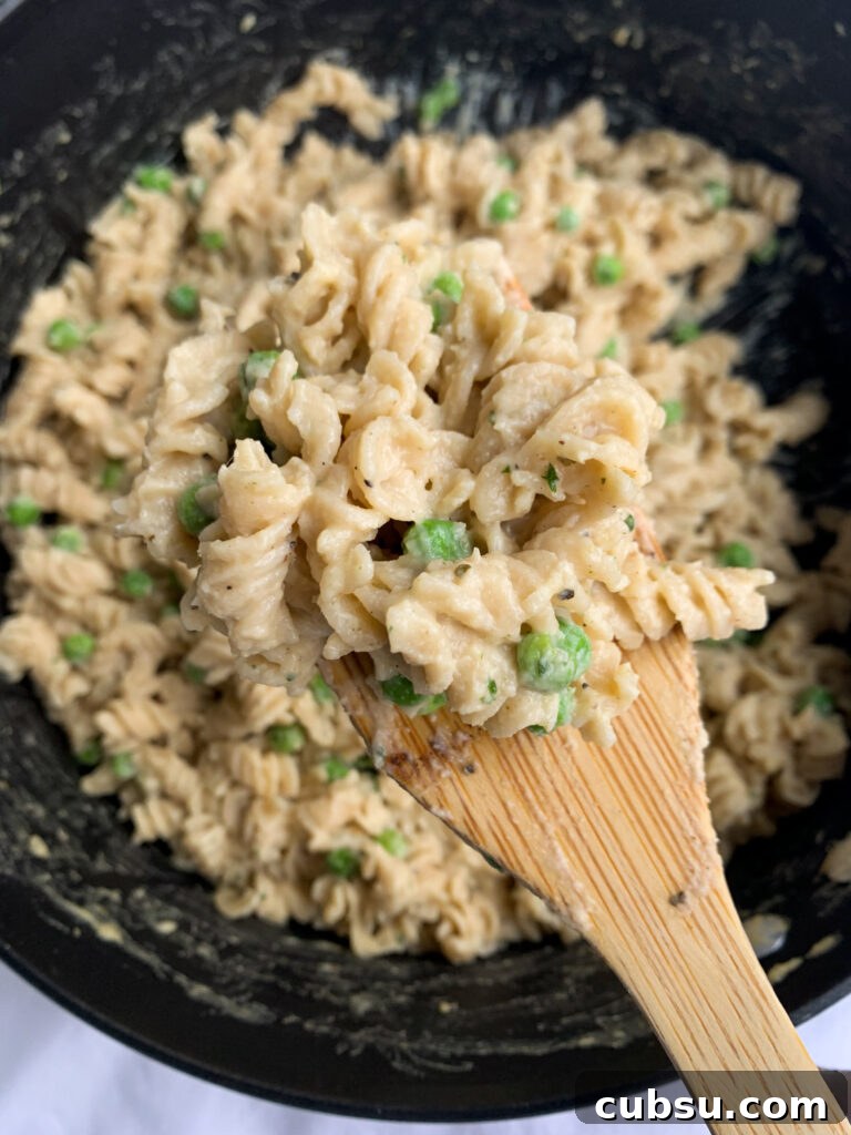 a pot of creamy cauliflower pasta with a wooden soon holding some of the pasta closer to the camera