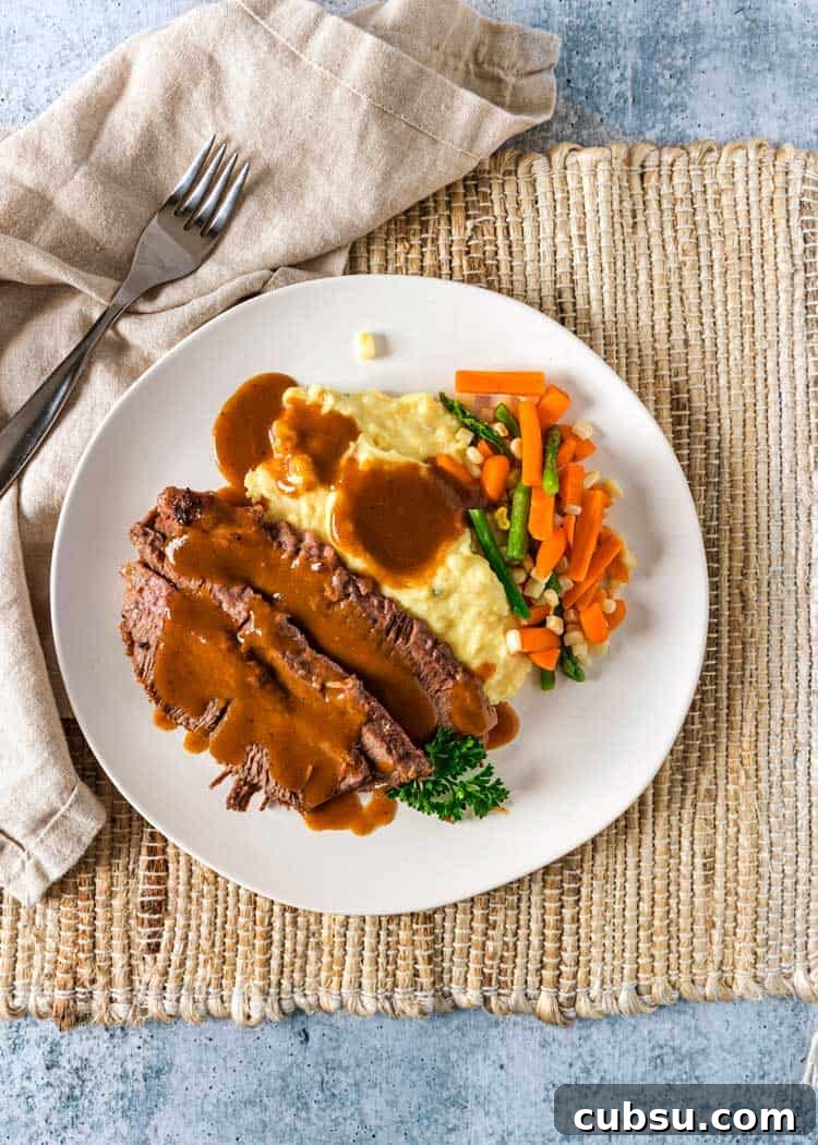Yankee Pot Roast starts with a pan seared, seasoned beef brisket that gets braised then served with vegetables and a gravy made from the braising liquid. overhead photo of Yankee Pot Roast on white plate