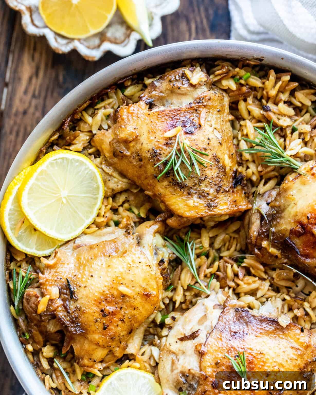 Rosemary Roasted Chicken with Creamy Parmesan Orzo 2 seared chicken thighs in a pan with lemons