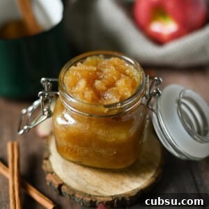 Applesauce in a clear jar with cinnamon sticks next to it.