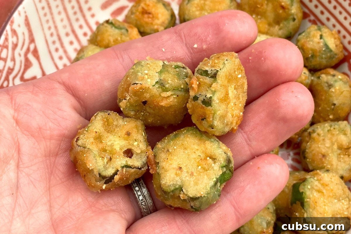 8 Must-Try Okra Recipes to Savor Before Summer Ends 10 A hand holding several golden-brown, crispy vegetable bites, with a patterned plate of more bites in the background.