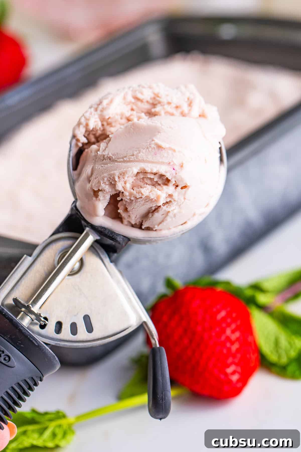an ice cream scoop holding up Strawberry ice cream in air