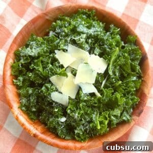 Massaged kale salad topped with shaved Parmesan and lemon dressing in a brown bowl on a orange checkered background.