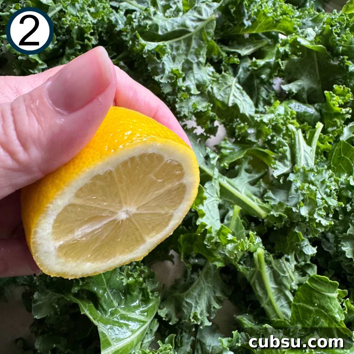Hand holding half of a lemon over kale leaves.
