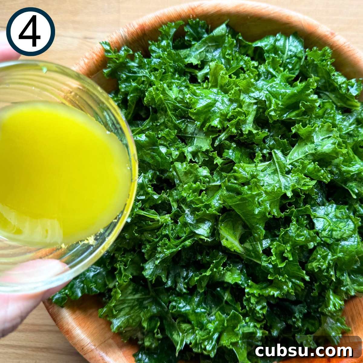 Lemon dressing being poured over massaged kale leaves.
