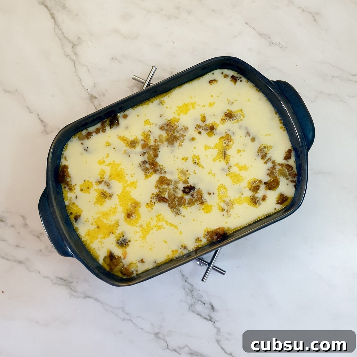 Egg and milk poured over half-baked bobotie in a baking dish.