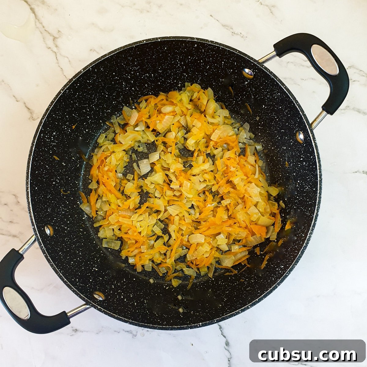 Diced onions and grated carrots frying in a frying pan.