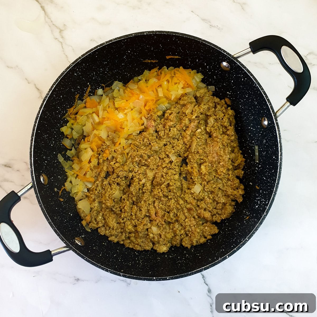 Bobotie mince and spices frying with carrots and onions in a frying pan.