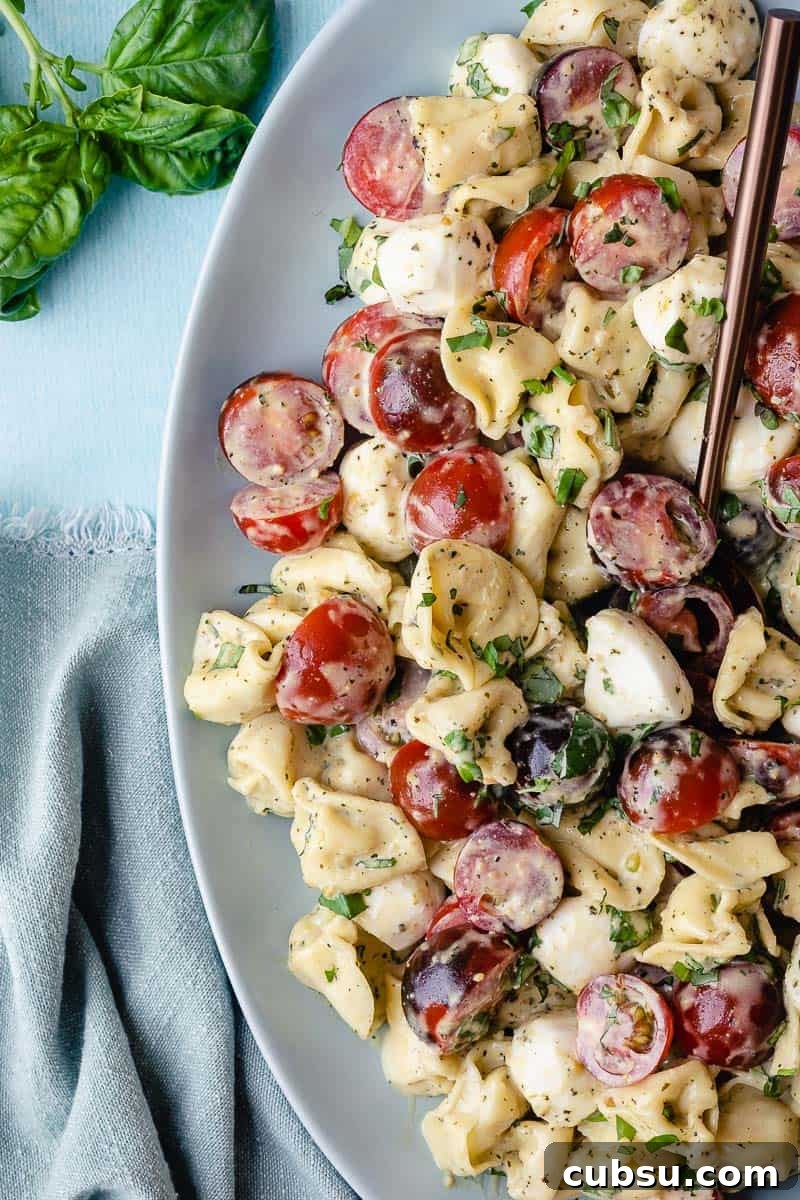 tortellini caprese salad in serving bowl next to basil and napkin