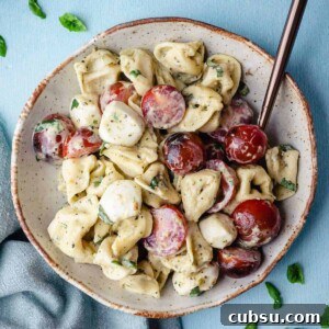 small bowl of tortellini caprese salad with spoon and basil leaves