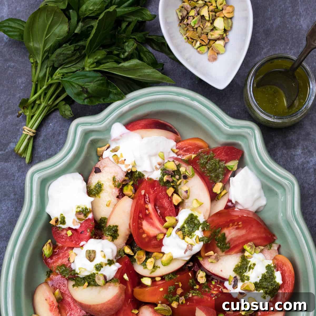 burrata caprese on green platter with basil, basil vinaigrette, and bowl of pistachios