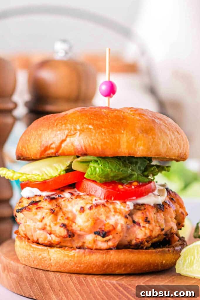 Side view of a grilled salmon burger stacked with toppings on a wooden board