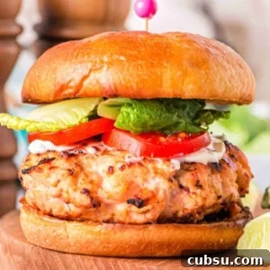 Square close-up of a grilled salmon burger on a brioche bun with lettuce, tomato, and mayo